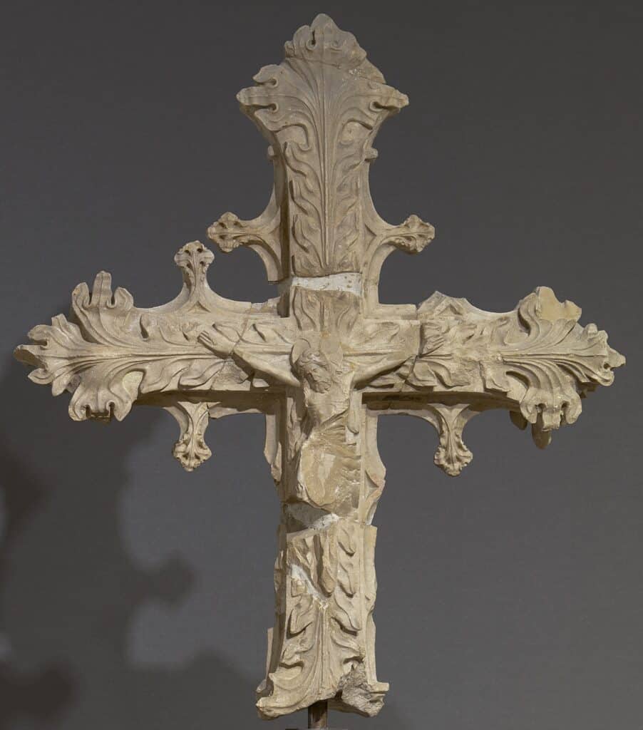 Creu de pedra gòtica amb Crist crucificat al centre i els braços decorats amb fullatge d'acant en relleu.