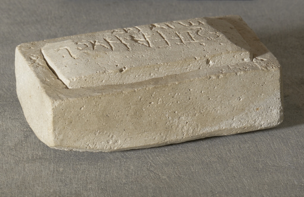 Lipsanoteca de pedra calcària de forma rectangular amb tapadora, decorada amb inscripcions llatines gravades en relleu als seus costats i a la tapa.