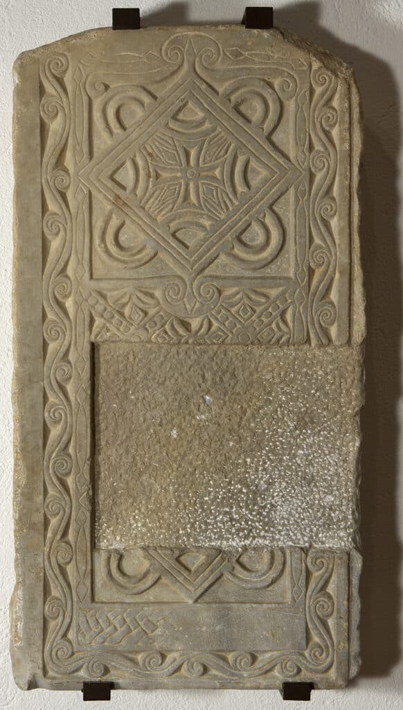 Cancell d'altar de pedra amb decoració geomètrica d'entrellaços i creu central en relleu, marc amb motius vegetals estilitzats