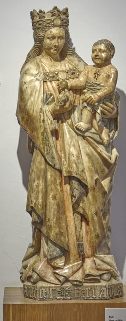 Escultura policromada d’estil gòtic representant una figura femenina coronada que sosté un infant als braços. Tots dos mostren expressions serenes. La figura vesteix llargues robes plegades i a la base hi ha una inscripció tallada. L’obra està situada sobre un suport de fusta davant d’una paret blanca