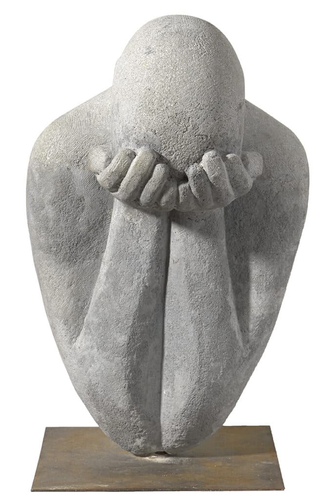 Escultura de figura abstracta amb cap inclinat i mans juntes cobrint el rostre, pedra grisa amb textura rugosa sobre pedestal.