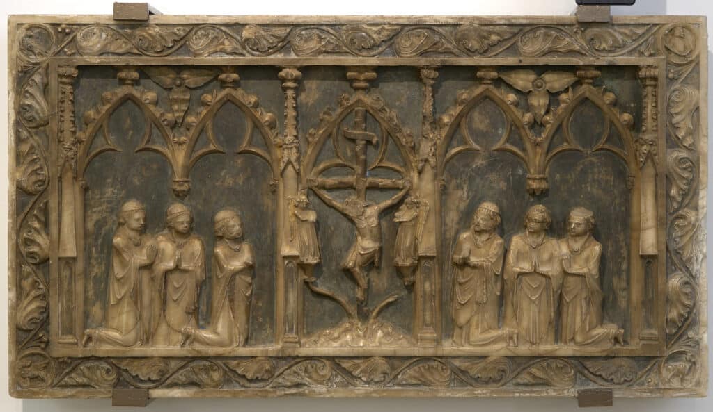 Relleu en pedra amb escena de Crucifixió central i grups de figures agenollades sota arcades gòtiques, marc amb decoració vegetal.