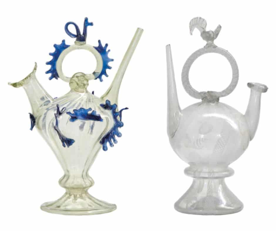 Dos càntirs decoratius de vidre amb nanses i aplicacions ornamentals, un amb decoració blava i l'altre transparent.