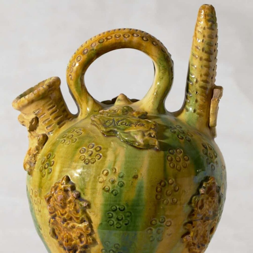 Càntir de ceràmica vidriada en tons verds i grocs amb decoració en relleu, nanses laterals i broc superior, estil tradicional català.