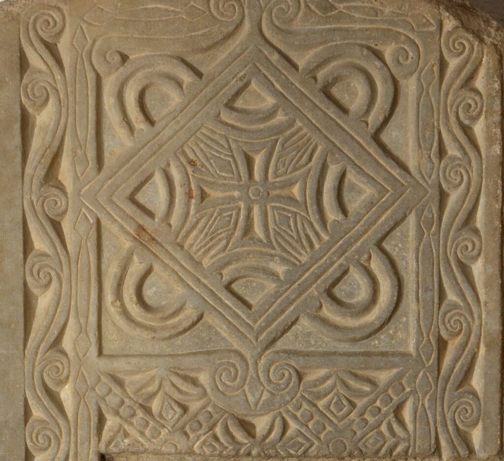 Cancell d'altar de pedra amb decoració geomètrica d'entrellaços i creu central en relleu, marc amb motius vegetals estilitzats